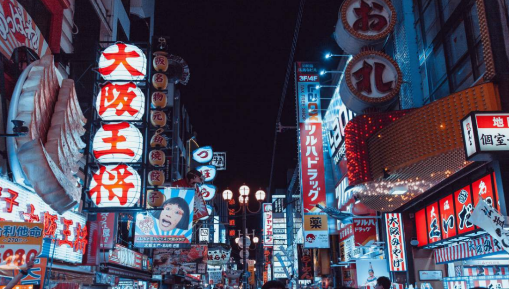 Brightly lit street in Osaka featuring neon signs and advertisements in Japanese characters at night.