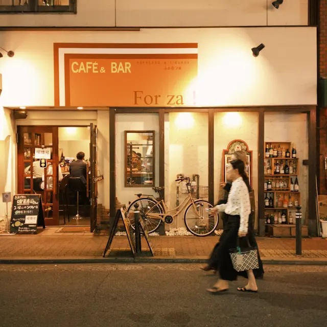 Exterior view of a café and bar named 'For za!' with a bicycle parked outside and a display of bottles on the wall.