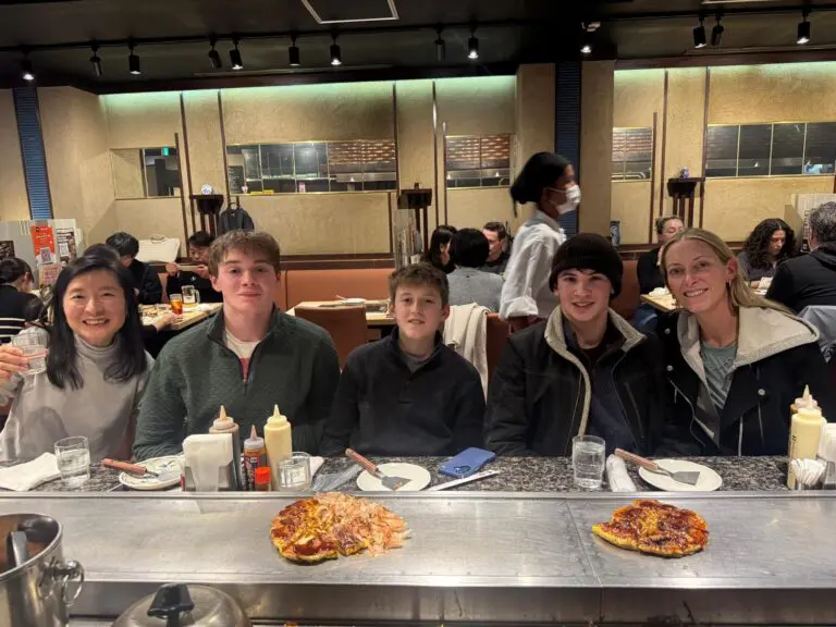 Group of five individuals seated at a table in a restaurant, with dishes of food in front of them.