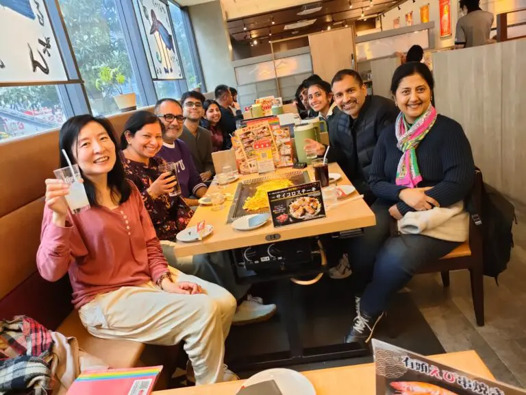 Group of seven people seated at a table in a restaurant, enjoying drinks and food together.