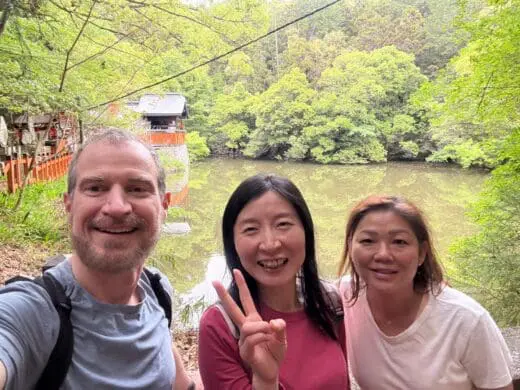 On a Kyoto Hidden Gems tour, Scott and Theresa smile by the Kodama Ike pond near Fushimi Inari Shrine, framed by lush green trees along a quiet trail.Kyoto Hidden Gems Tour