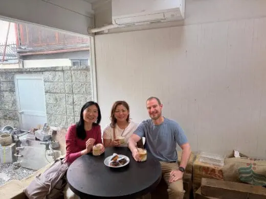 Scott and Theresa at a Kyoto hidden gems walking tour cafe table, smiling while holding drinks, seated indoors beside a stone wall.