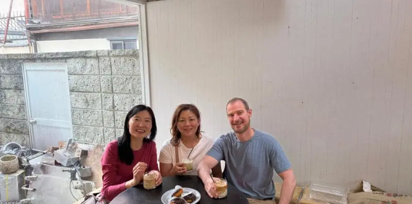Scott and Theresa at a Kyoto hidden gems walking tour cafe table, smiling while holding drinks, seated indoors beside a stone wall.