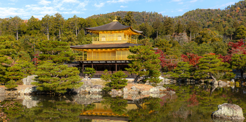 Kiyomizu-dera temple pagoda framed by crimson and orange autumn foliage against a bright blue Kyoto sky, capturing Kyoto’s historic fall scenery in Japan.