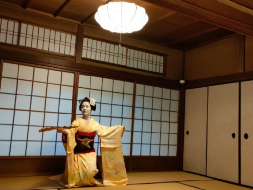 Kyoto geisha in a yellow kimono performs a traditional dance inside a tatami room with shoji screens, in the Gion district of Kyoto.