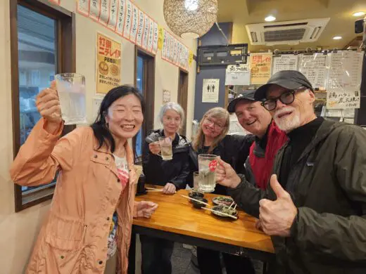 Tenma, Osaka izakaya interior with a wooden table, friends toasting with beer glasses, hanging Japanese menu signs, warm lighting.Osaka hidden gems food tour
