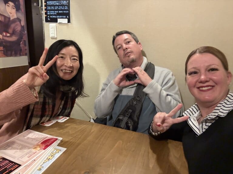 whatsapp-image-2025-06-29-at-06-49-10_24428ebe Three individuals posing together with peace signs and heart gestures in a casual indoor setting.
