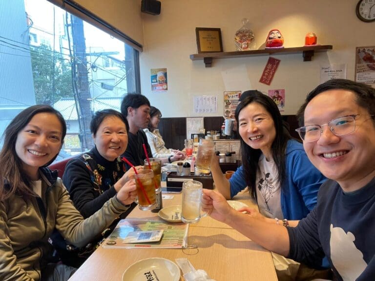 whatsapp-image-2025-07-15-at-10-26-48-am-3 Group of four people in a restaurant raising glasses for a toast, with drinks in hand.