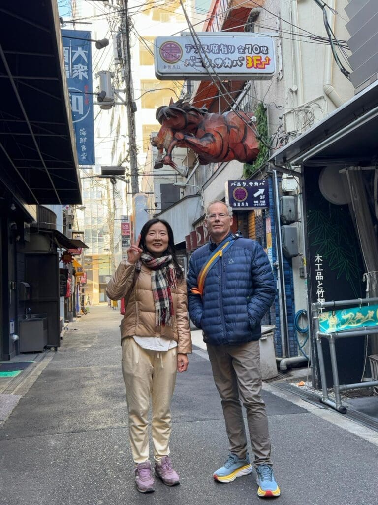 whatsapp-image-2025-07-15-at-10-26-49-am-1 Two individuals standing in a narrow alley with a large crab sign overhead in an urban setting.