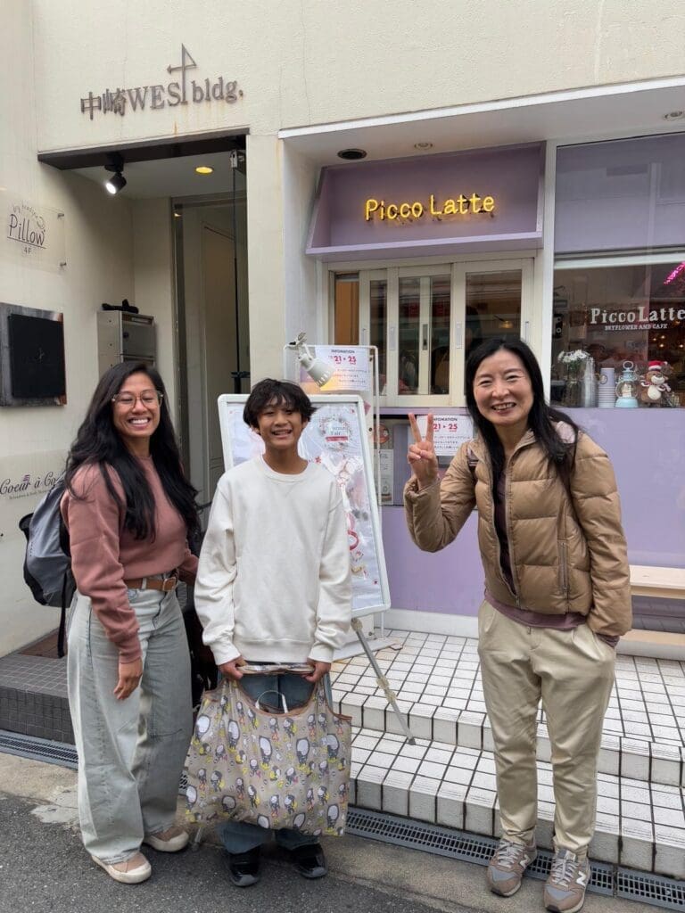 Three individuals standing outside a café named Picco Latte, with a sign displaying the café's name.
