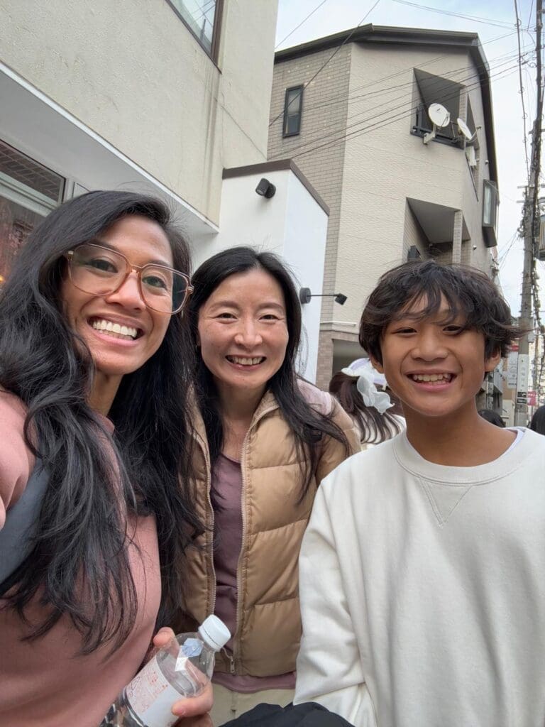 whatsapp-image-2025-07-15-at-10-26-50-am Three individuals smiling for a selfie outdoors, with one holding a water bottle and wearing glasses.