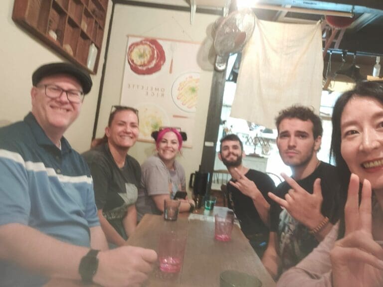 Group of five individuals seated at a table in a casual dining setting, smiling and posing for the camera.