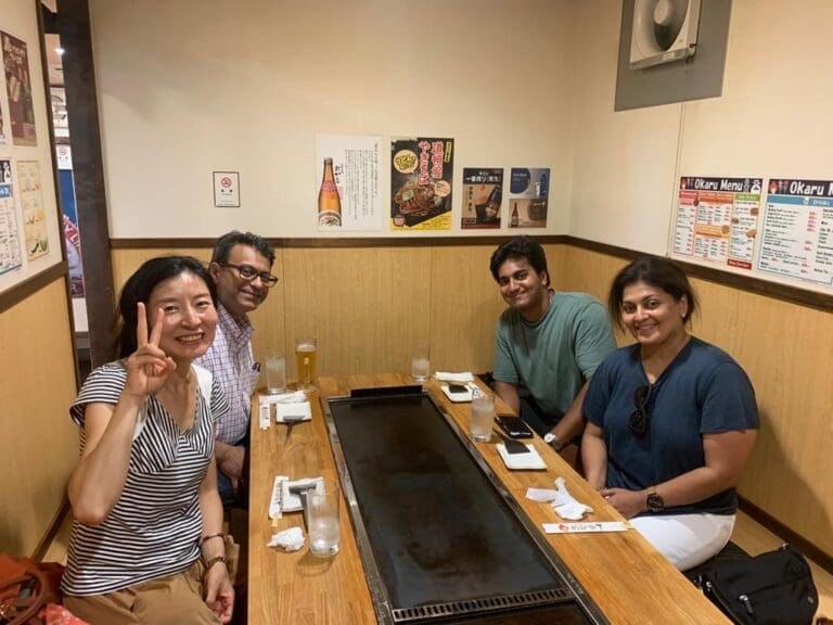 whatsapp-image-2025-07-15-at-10-26-54-am-1 Group of four people seated at a table in a restaurant with a grill in the center.