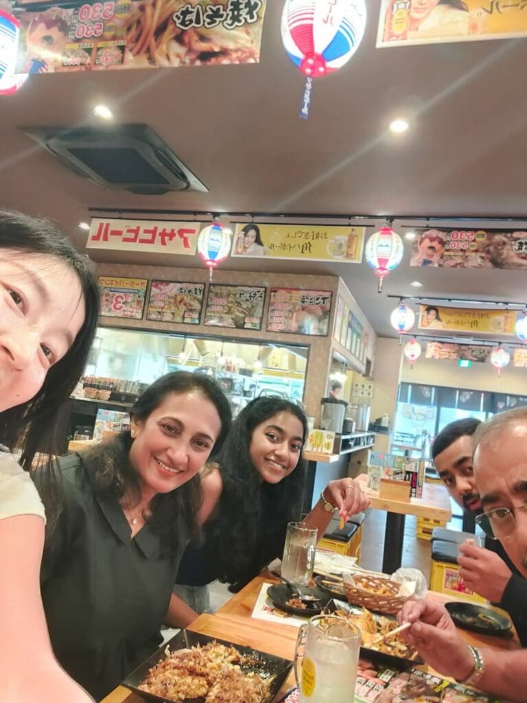 whatsapp-image-2025-07-15-at-10-26-56-am Group of five people enjoying a meal together in a restaurant with colorful lanterns and menu displays.