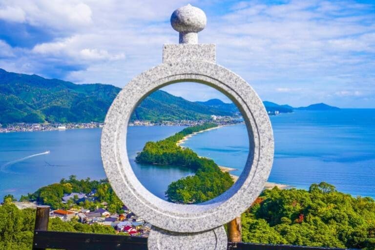 Granite circular frame overlooking Amanohashidate, a scenic sandbar in Japan surrounded by mountains and water.