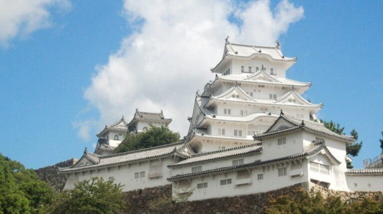 Himeji Castle, a historic Japanese castle with multiple white structures and intricate roof designs against a blue sky.