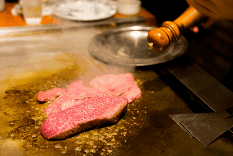 image-81 Kobe beef restaurants, Raw beef steak being cooked on a hot grill with steam rising.