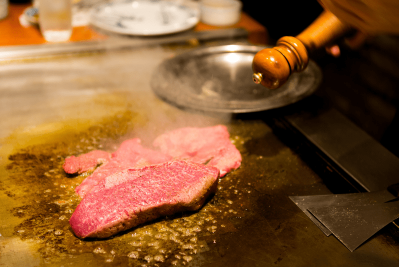 Kansai Travel Blogs 16 Kobe beef restaurants, Raw beef steak being cooked on a hot grill with steam rising.