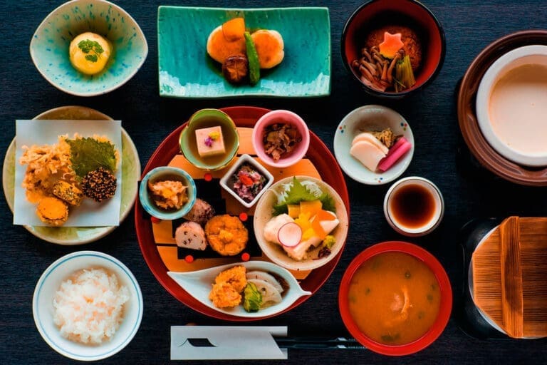 15 Traditional Food in Kyoto Dishes You Need to Taste 2 A colorful Japanese kaiseki meal, showcasing Traditional Food in Kyoto, is arranged on a table with rice, soup, pickles, vegetables, tofu, and regional specialties—each beautifully presented in bowls and plates. Chopsticks and a napkin are placed in front.