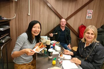Three individuals enjoying a meal together at a dining table, smiling and holding food plates.