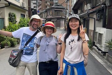 Three individuals posing for a photo on a street, with one making a peace sign and wearing a hat.