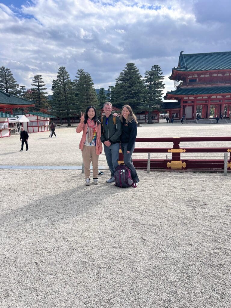 Three individuals posing together at Heian Shrine in Kyoto, Japan, with traditional architecture in the background.