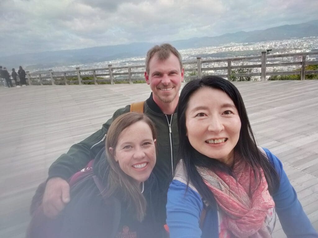 Three individuals posing for a selfie at a viewpoint with a cityscape in the background.