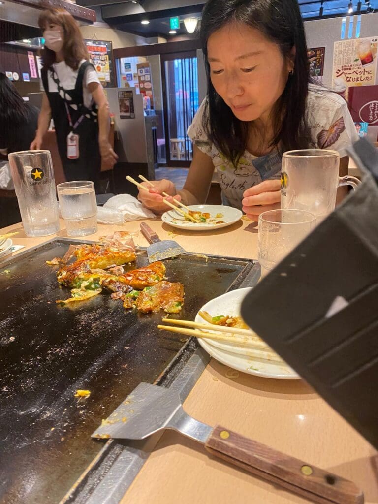 Woman eating at a table with plates and chopsticks in a restaurant setting.