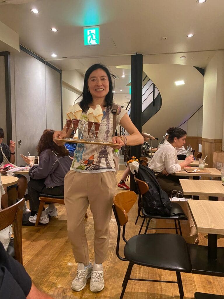 Woman holding a tray with multiple ice cream cones in a casual indoor setting.