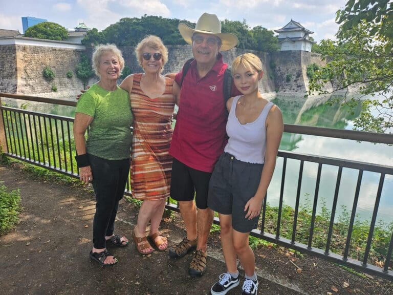 photo-with-shawn-at-the-osaka-castle-3 Group of four people posing together at Osaka Castle with a moat in the background.
