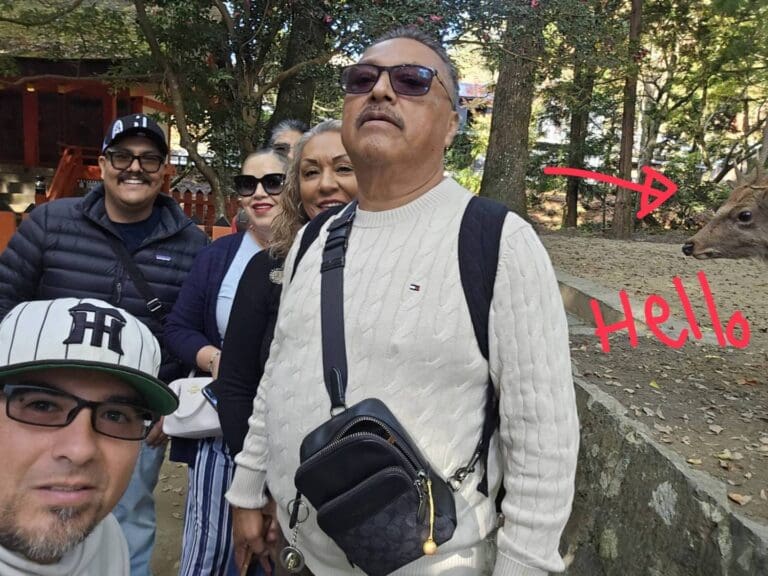 the-photo-by-maru-with-guests-in-nara Group of visitors posing for a photo with a deer in Nara, Japan, in a natural outdoor setting.