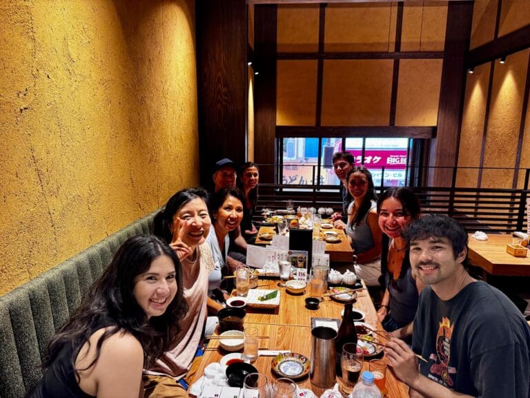 Group of people sitting around a wooden table in a restaurant, enjoying a meal together.