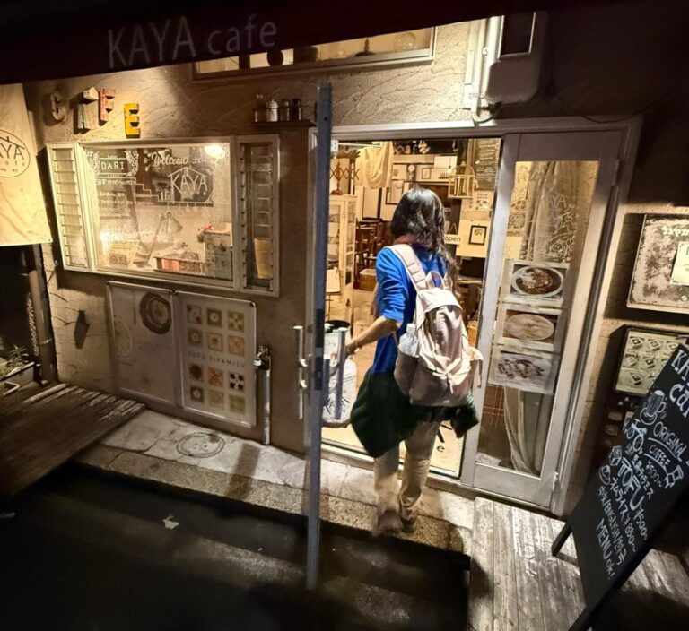 Person entering Kaya cafe, wearing a backpack, with cafe signage and menu displayed outside the entrance.